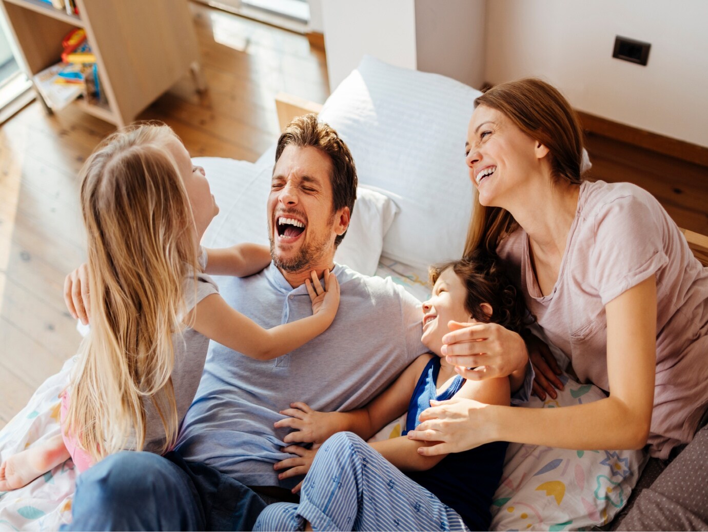 Family of four laugh and play on bed of home equipped with a YORK Heat Pump for dependable performance throughout all seasons.