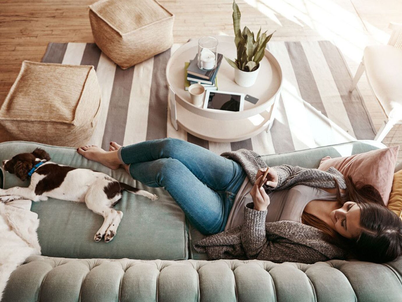 A woman relaxing on the sofa with her dog and using a mobile phone