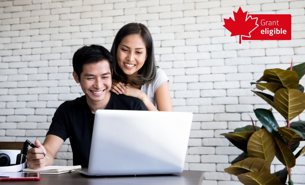 A man and a woman looking at a laptop near a white brick wall.